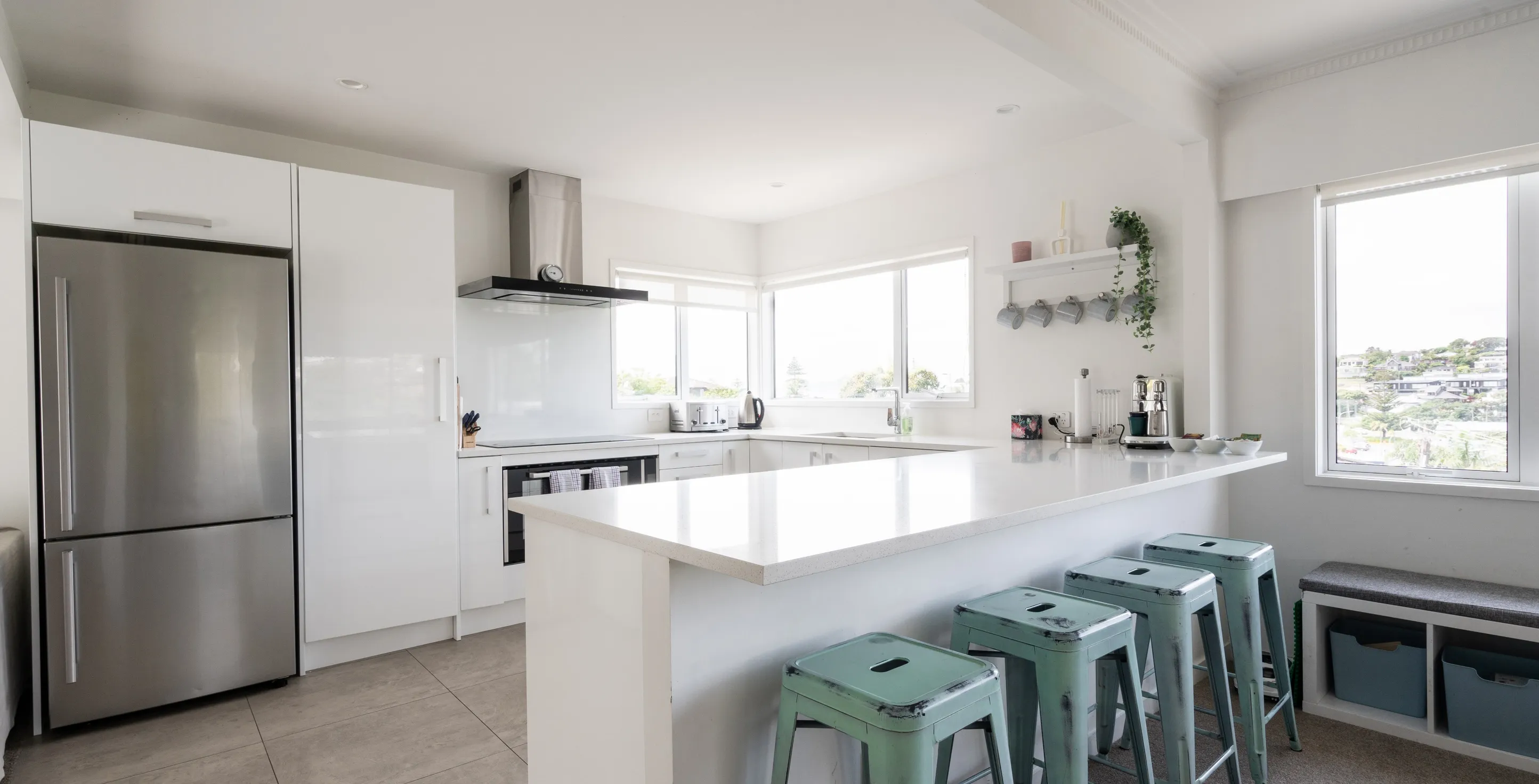 The same kitchen, spotless: bare white counters, an empty island, stools tucked in and nothing left out. What the messy kitchen becomes after the cleanup.